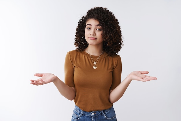 Not big deal. Unbothered careless stylish young modern female curly dark hair shrugging hands spread sideways smirking unaware look confused clueless, cannot help no idea shrugging, white background
