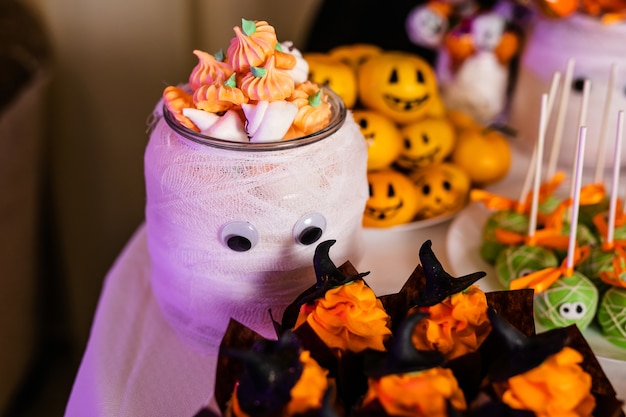 Big decorated jar with pumpkin marshmallows on the candy bar for the celebration of Halloween.