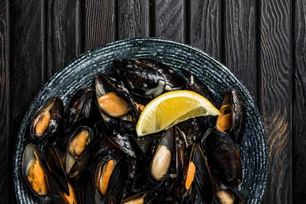 A big dish of mussels with sauce grilled white bread and a slice of lemon shot from above dark wooden backdrop closeup