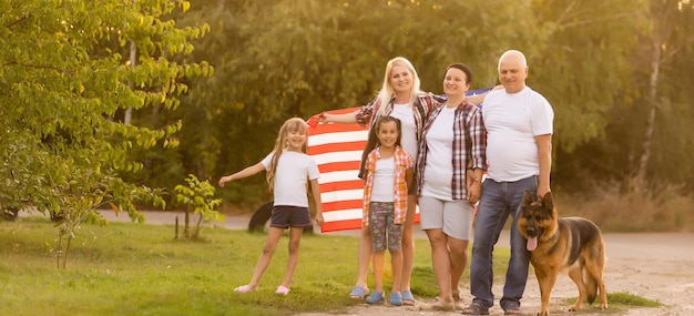 big family are walking walking american flags. Front view, american patriots on the park meadow.