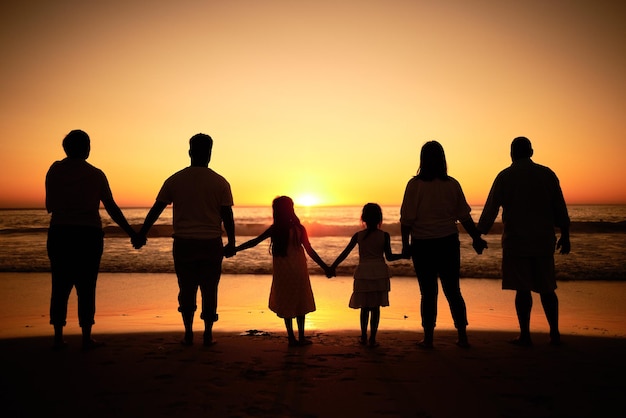 Big family silhouette on beach with sea waves sunset on the horizon and holding hands for development wellness support and love Children and group of people watch ocean on dark orange sky mockup