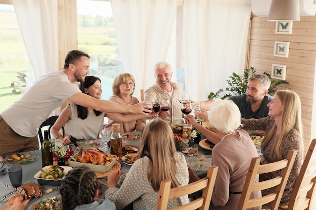 테이블에 앉아 저녁 식사를 위해 휴가를 축하하는 레드 와인 잔으로 토스트하는 대가족