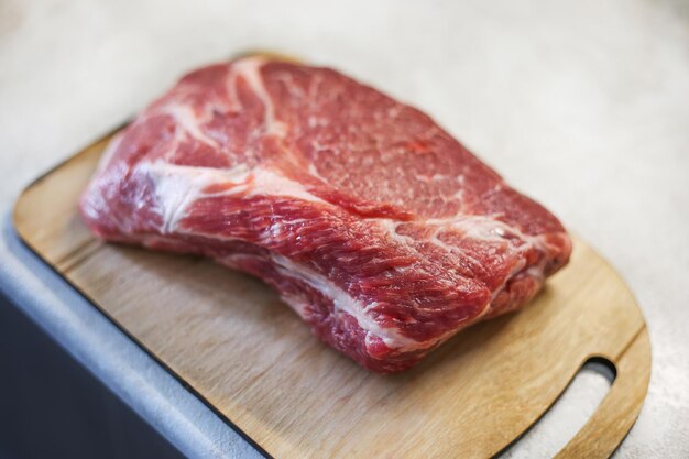 Big fresh piece of meat on wooden cutting board on light kitchen table