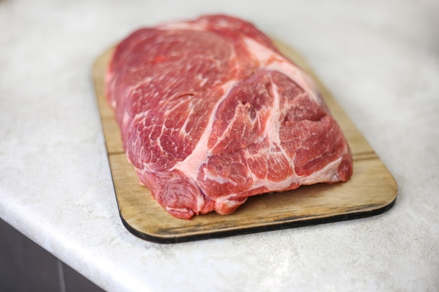 Big fresh piece of meat on wooden cutting board on light kitchen table