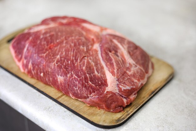 Big fresh piece of meat on wooden cutting board on light kitchen table