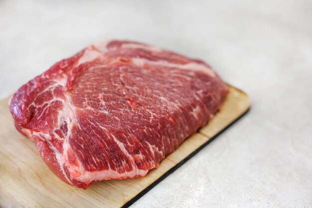 Big fresh piece of meat on wooden cutting board on light kitchen table