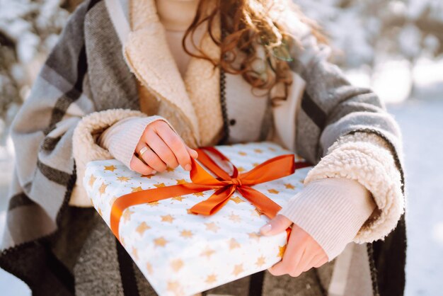 女性の手に赤いリボンが付いた大きなギフトボックス。クリスマスプレゼントを持っているファッションの若い女性。