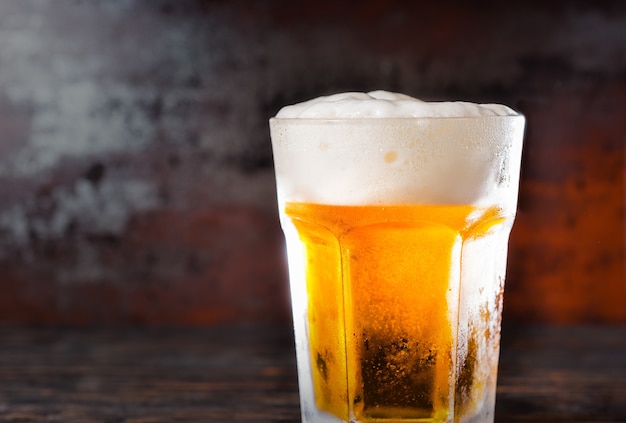 Big glass with a light beer and a head of foam on old dark desk. Drink and beverages concept