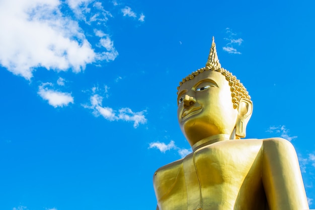 Big golden Buddha statue with blue sky background.