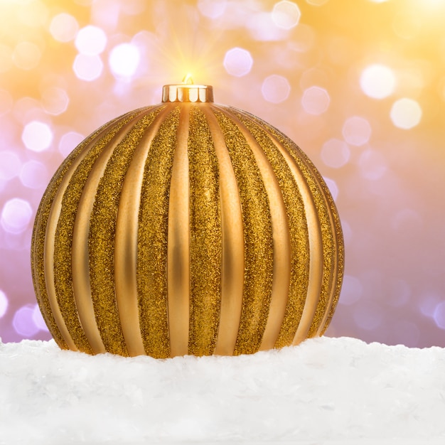 Big golden Christmas ball on snow over festive defocused background with copy-space