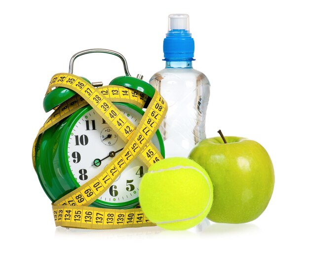 Big green alarm clock with tennis ball and bottle of water isolated on white background