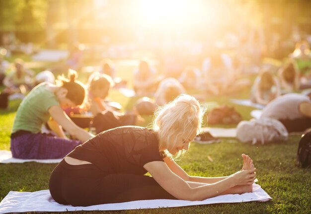 Big group of adults attending a yoga class outside in park