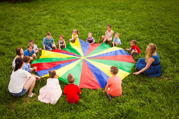 Большая группа детей, играющих в парашютную игру на зеленом поле