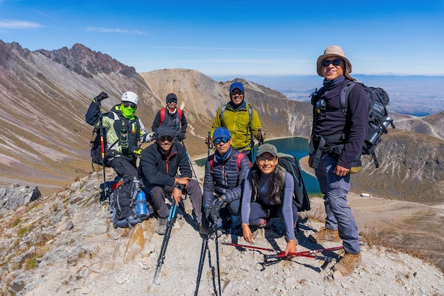 Big group of people having fun in success pose on mountain top against lakes and mountains