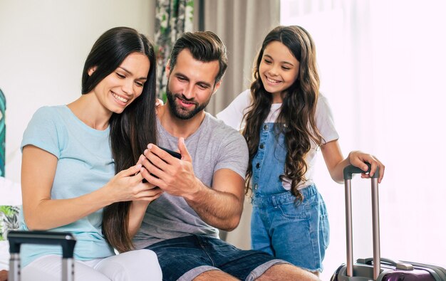 Una grande famiglia di turisti felici ed entusiasti utilizza uno smartphone mentre sono seduti sul letto nella camera d'albergo