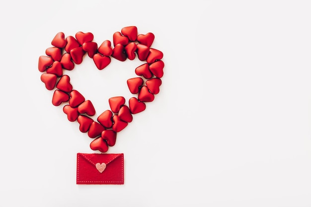 Фото Большое сердце из маленьких красных сердечек и войлочный конверт на белом фоне, вид сверху