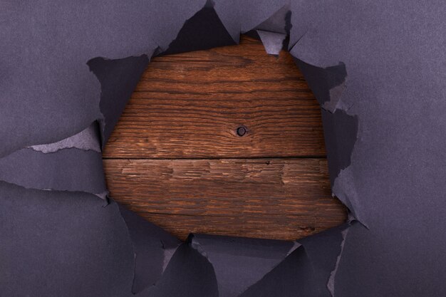 Big hole in the black paper. Torn. Wooden background. Abstract background.