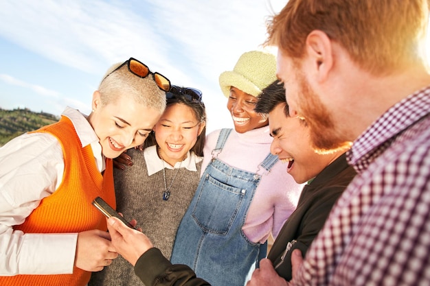 Foto grandi risate di amici multirazziali che usano il cellulare, persone intrattenute dai social media.