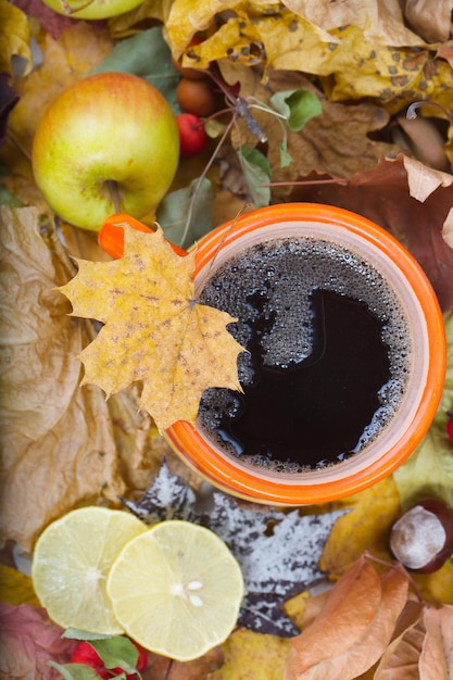 Big orange cup with hot tea on dried leaves