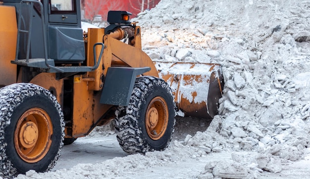 Big orange tractor cleans up snow from the road Cleaning and cleaning of roads in the city from