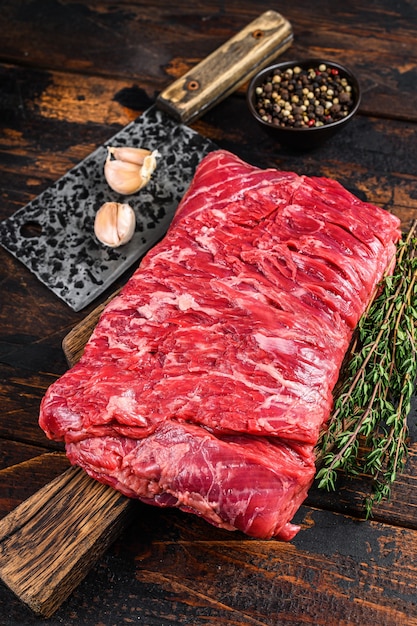 Big piece of raw beef brisket cut meat with herbs and butcher
cleaver. dark wooden background. top view.