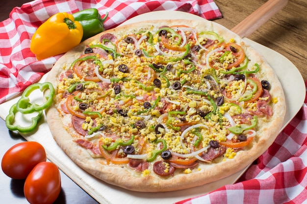 Big pizza "portuguesa" with bell peppers and plaid towel on wooden table