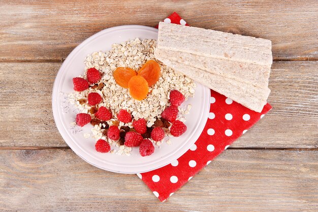 Piatto grande con farina d'avena, piccole pagnotte di pane e bacche su un tovagliolo a pois su fondo in legno