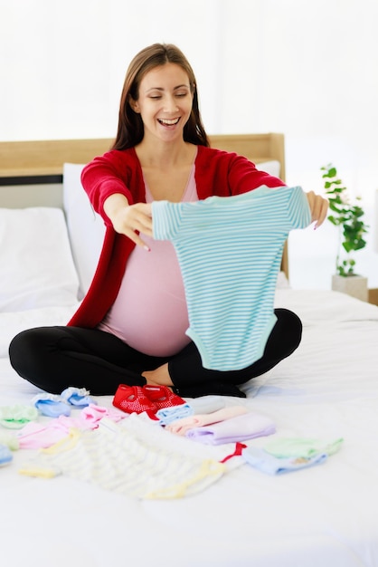 A big pregnant woman is happily preparing baby clothes on her stomach