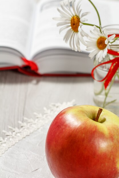 Foto grande mela rossa con libro aperto e camomille sullo sfondo