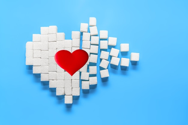 Big red heart on broken heart made of sugar cubes on a blue background.