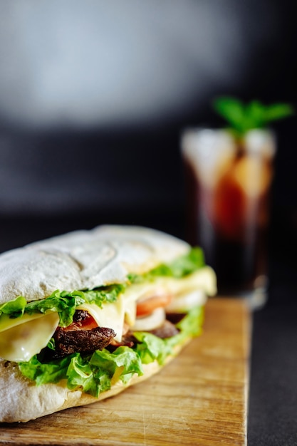 Big sandwich for couple on black background rosemary cucumber wooden board Street food, fast food. Homemade burgers with beef, cheese on the wooden table. Glass of cola with ice, mint