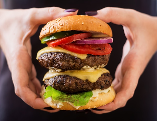 Big sandwich - hamburger burger with beef, cheese, tomato and tartar sauce in female hands