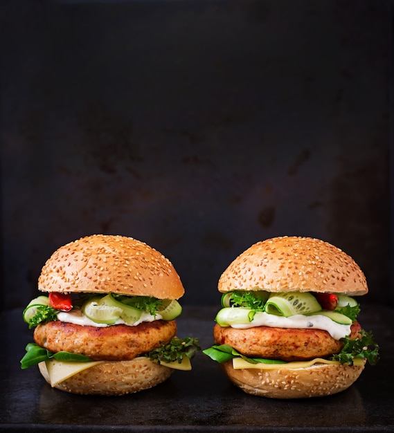 Big sandwich - hamburger with juicy chicken burger, cheese, cucumber, chili and tartar sauce on black background