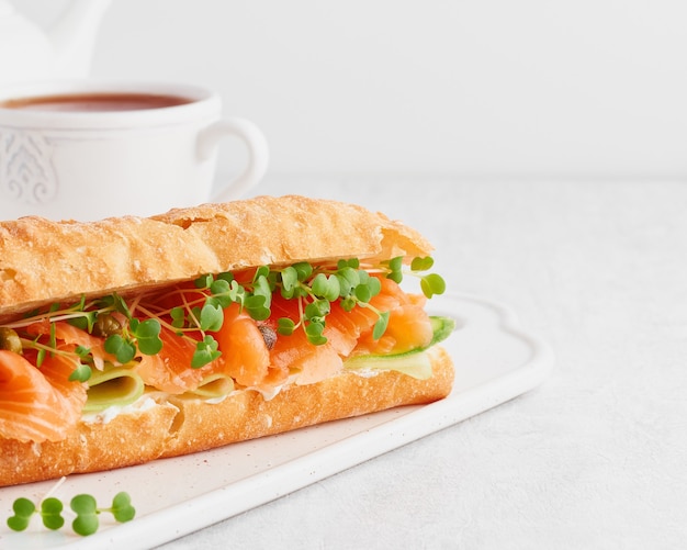 Big sandwich with salmon, cream cheese and cucumber slices on white concrete table