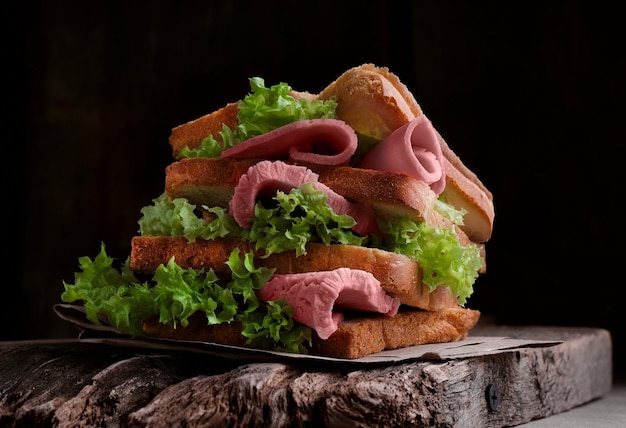 Big sandwich witn green leaves and beef on wooden board black background