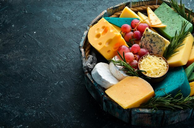 Big set of cheeses with snacks in a wooden box On a black stone background Free copy space