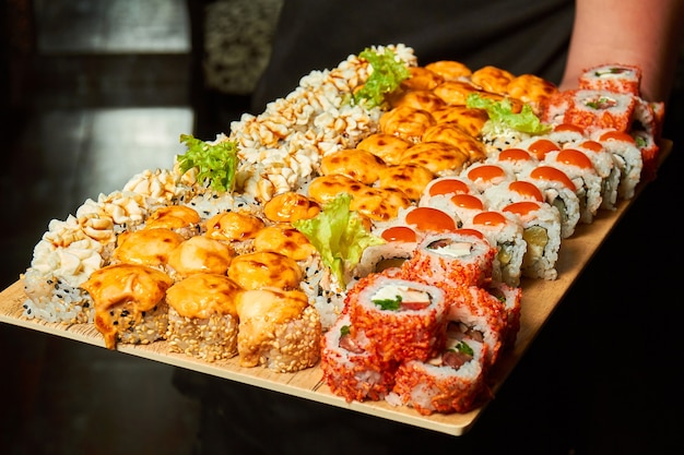 Big set of sushi rolls on a board in the hands of a waiter