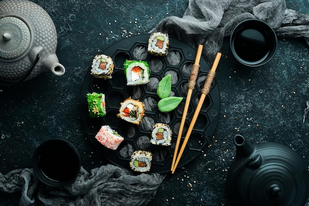 Большой набор суши-роллов с морепродуктами на фоне черного камня Вид сверху Свободное место для текста