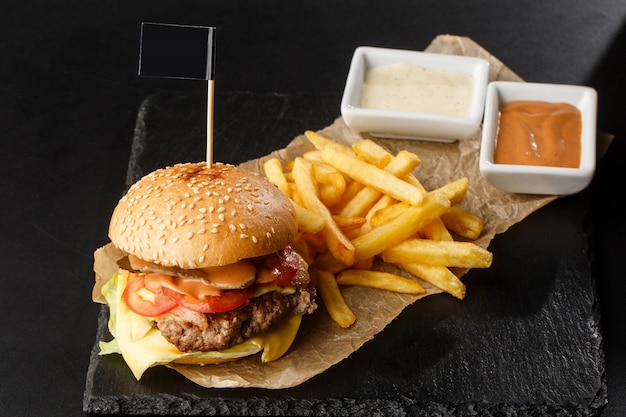 Big single cheeseburger with french fries isolated on black