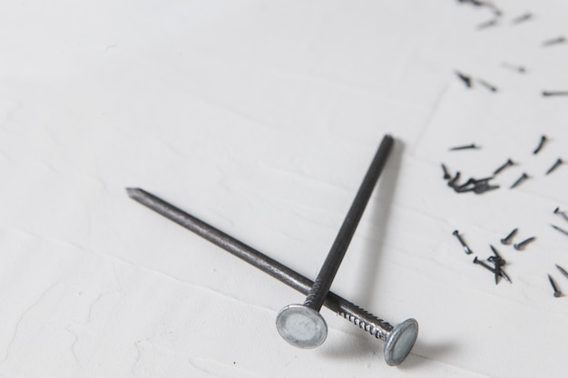 Big and small building nails on white plaster background