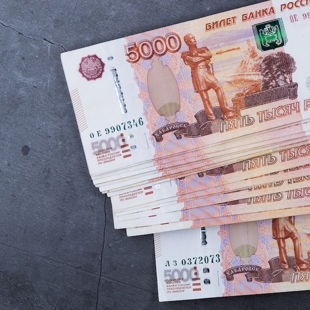 Big stack of Russian money banknotes of five thousand rubles lying on a grey cement.