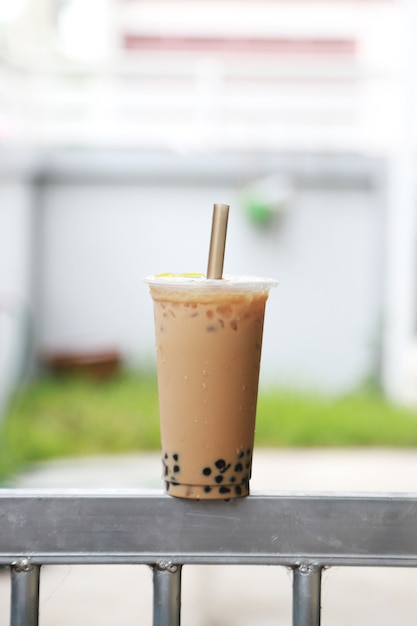 Big and tall cup iced milk tea wih bubble boba fresh and sweet drink Taiwan style put on the steel bar and blur background , food and drink concept