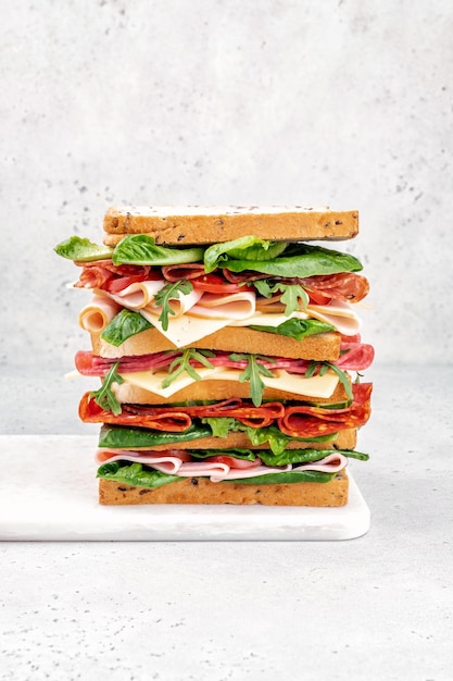 Big tasty sandwich with ham salami salad cheese and tomatoes on white background