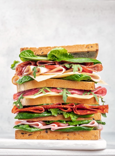 Grande panino gustoso con prosciutto, salame, insalata, formaggio e pomodori