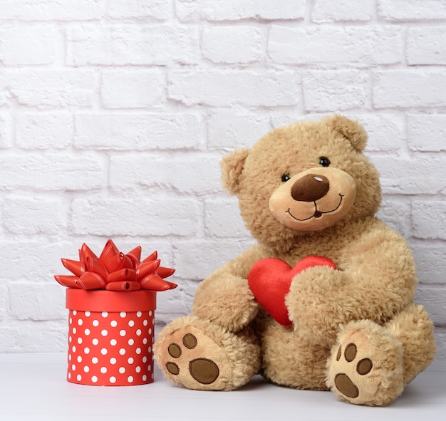 Big teddy bear and cardboard box with red bow on white brick wall background