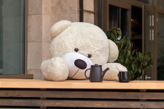 Foto un grande orso giocattolo è seduto al bancone di un bar con una tazza di tè e una teiera