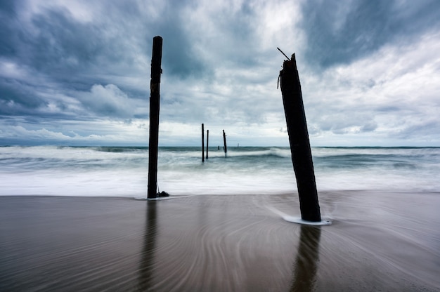 Большая волна обрушивается на разрушающийся деревянный мост на пляже в штормовую погоду на пляже Пилаи, Пхангнга, Таиланд