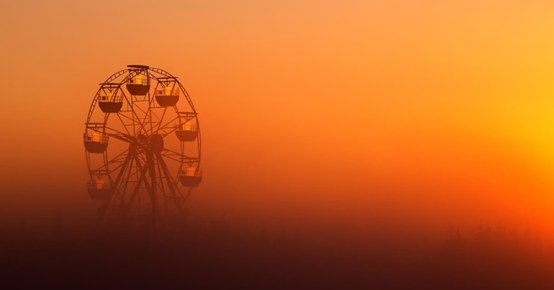 Big white Ferris wheel in a foggy park at dawn.