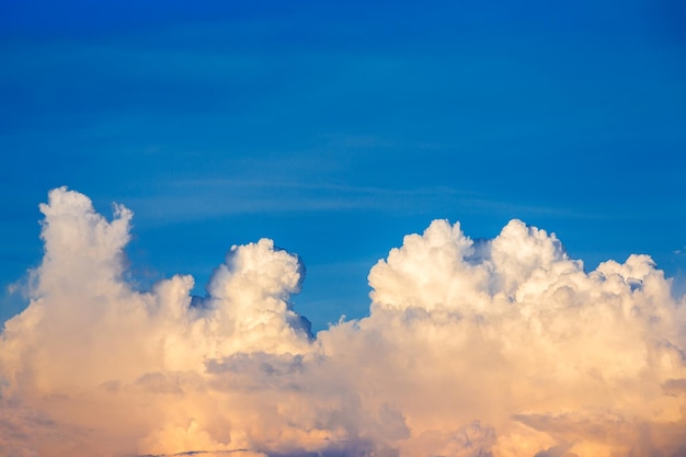 Big White fluffy cumulonimbus storm clouds in deep blue sky at sunset