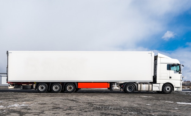 A big white truck with a white trailer standing on the countryside road in against a blue sky with clouds. Transportation concept